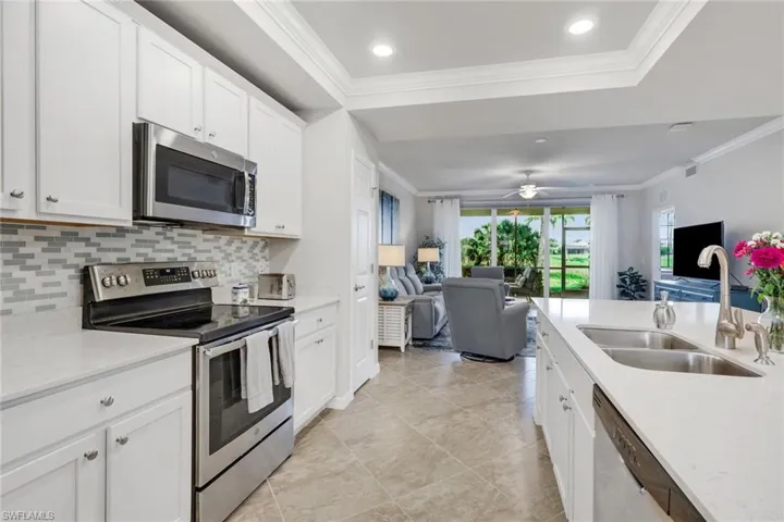 Kitchen with stainless steel appliances, open floor plan, crown molding, light stone counters, and white cabinetry