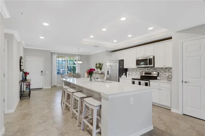 Kitchen with a kitchen bar, stainless steel appliances, a large island with sink, white cabinetry, and backsplash