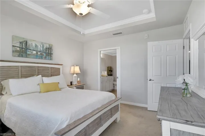 Bedroom with light carpet, crown molding, a raised ceiling, a ceiling fan, and ensuite bath