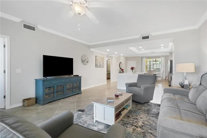 Living room featuring light tile patterned flooring, crown molding, a raised ceiling, ceiling fan, and hanging lights