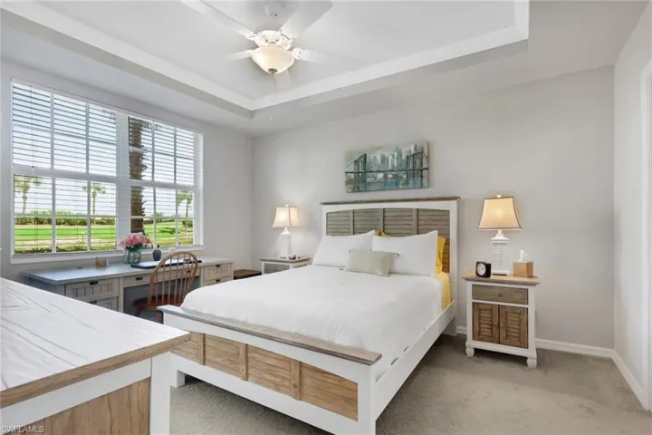 Bedroom featuring ceiling fan, light carpet, and a tray ceiling