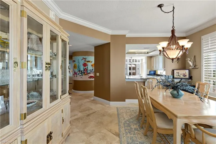 Dining room with a textured ceiling, a chandelier, crown molding and travertine tile