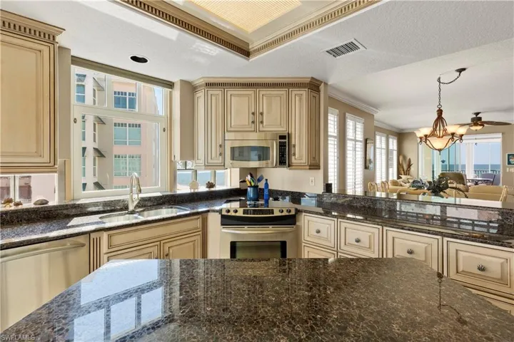 Kitchen featuring dark stone countertops, crown molding, stainless steel appliances, hanging light fixtures, and a chandelier