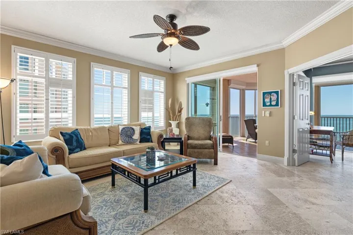 Living room featuring ornamental molding, a textured ceiling, plenty of natural light, ceiling fan, and stone tile flooring