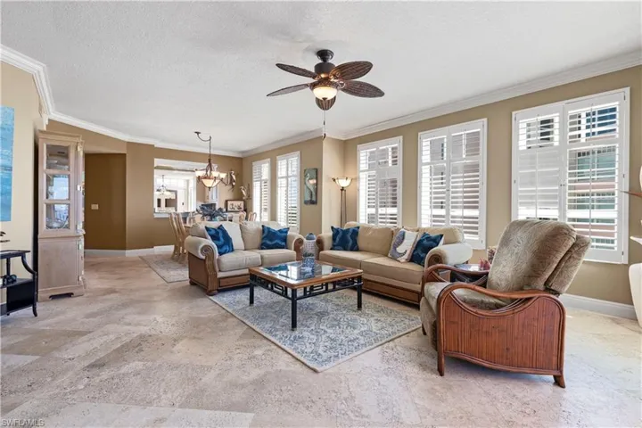 Living room with ornamental molding, a textured ceiling, ceiling fan, plantation shutters and a chandelier