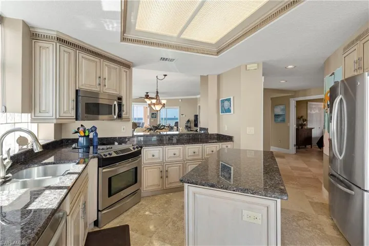Kitchen featuring appliances with stainless steel finishes, dark stone countertops, pendant lighting, a chandelier, and a textured ceiling