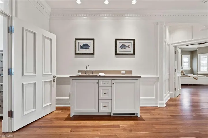 Bar featuring light wood-style floors, a decorative wall, wet bar, ornamental molding, and a sink