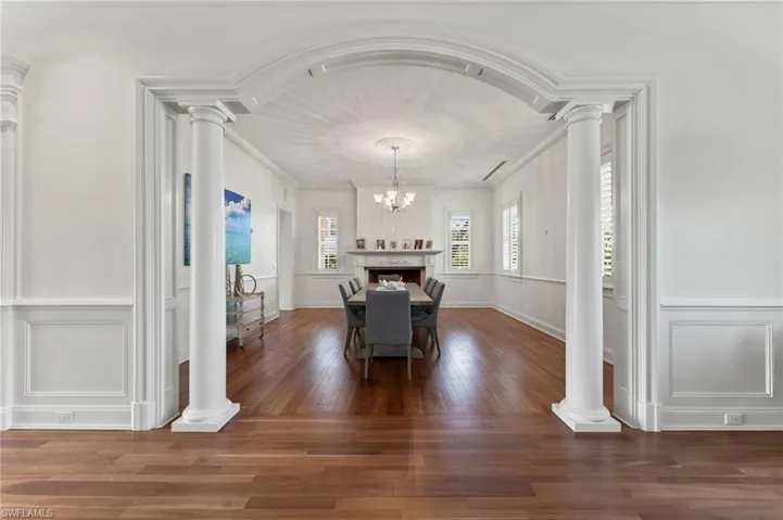 Dining room with an inviting chandelier, ornamental molding, decorative columns, a decorative wall, and wood finished floors