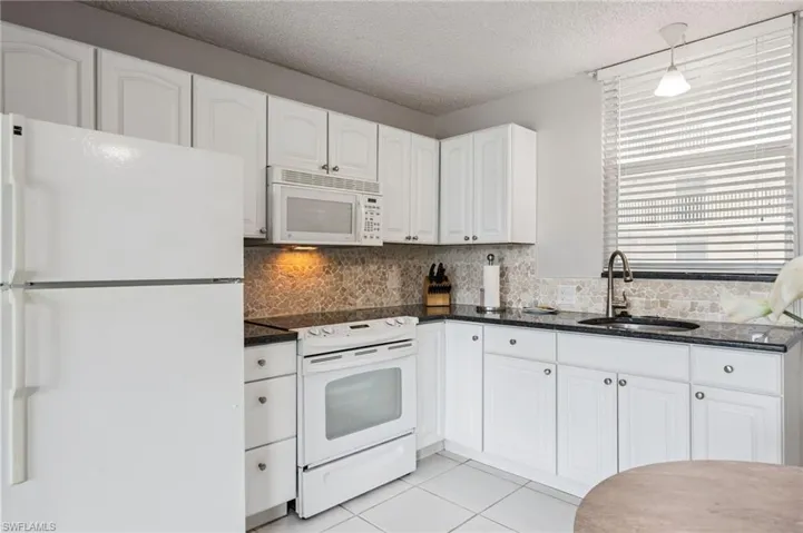 White cabinetry, dark granite countertops, a mosaic tile backsplash, and a window with blinds