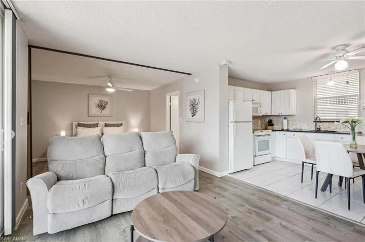 Open-concept living space with wood-finish flooring, a kitchen featuring white cabinetry and appliances, and a tiled dining area