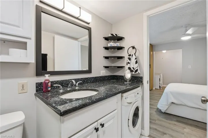 Vanity with dark countertop and integrated sink, chrome faucet, and white cabinetry and washer