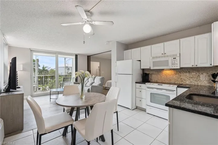 White cabinetry, dark granite countertops, tile flooring, and a stone-tiled backsplash define the kitchen space