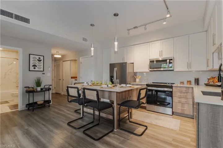 Kitchen with appliances with stainless steel finishes, light wood finished floors, pendant lighting, and light stone counters