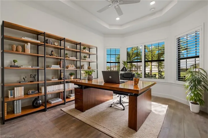 Home office with hardwood / wood-style floors, a tray ceiling, and ceiling fan