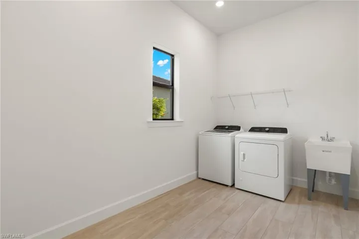 Clothes washing area featuring washing machine and clothes dryer, sink, and light wood-type flooring