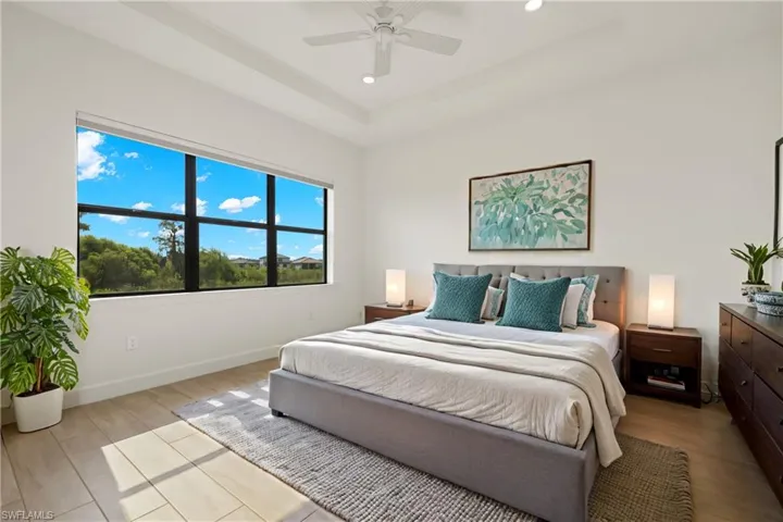 Virtually staged bedroom featuring a tray ceiling, ceiling fan, and light wood-type flooring