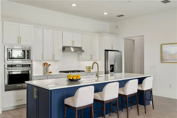 Virtually staged Kitchen featuring white cabinetry, appliances with stainless steel finishes, a kitchen bar, and a center island with sink