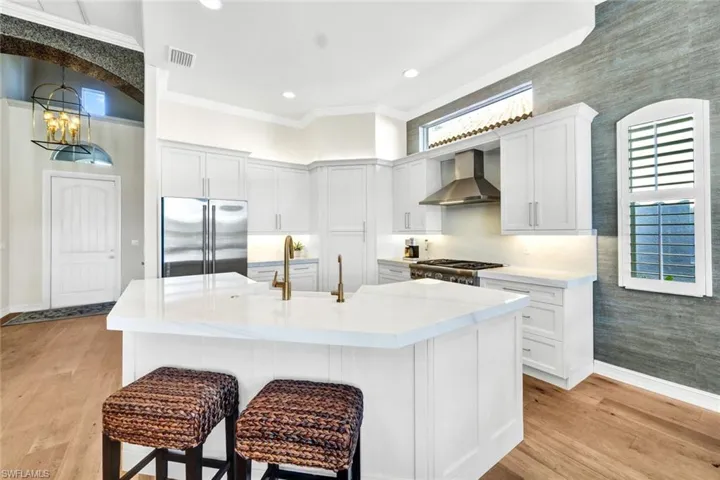 Kitchen with appliances with stainless steel finishes, wall chimney exhaust hood, a center island with sink, light hardwood / wood-style flooring, and white cabinets