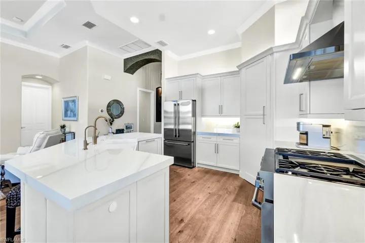 Kitchen with sink, wall chimney range hood, stainless steel appliances, and a kitchen island with sink