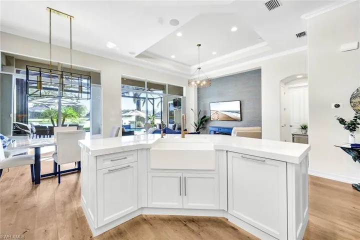 Kitchen with sink, an island with sink, decorative light fixtures, white cabinets, and light wood-type flooring