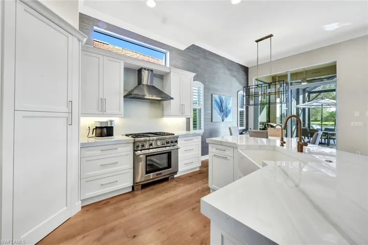 Kitchen featuring stainless steel range, sink, wall chimney range hood, decorative light fixtures, and white cabinets
