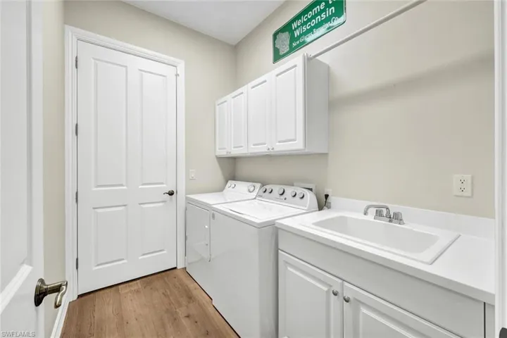 Laundry area with cabinets, sink, light hardwood / wood-style flooring, and washing machine and clothes dryer