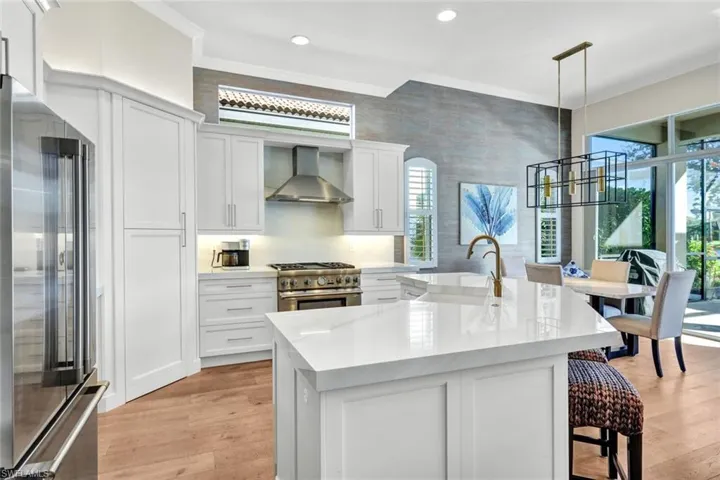Kitchen with plenty of natural light, wall chimney range hood, stainless steel appliances, and a kitchen island with sink