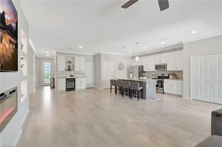 Living area featuring ceiling fan, wine cooler, recessed lighting, and ornamental molding