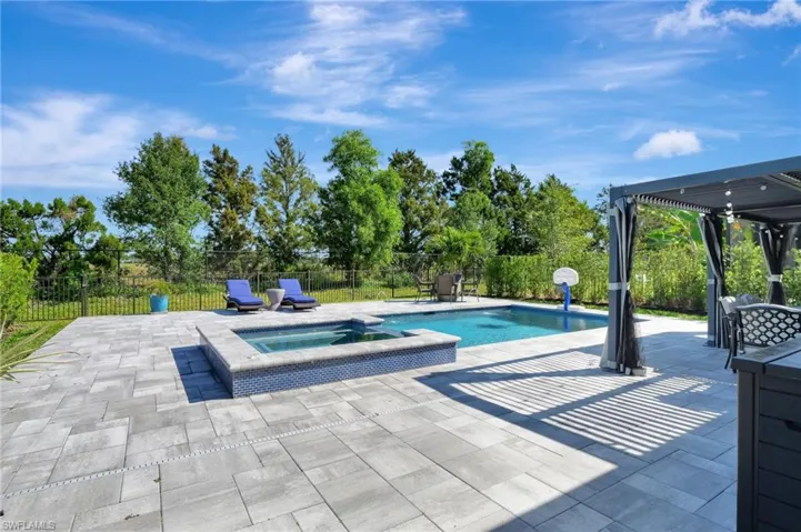 View of swimming pool with a patio, fence, and a pool with connected hot tub