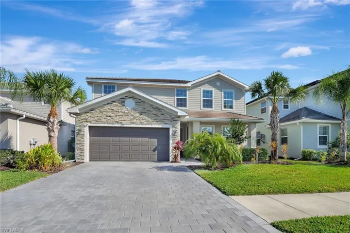 Traditional-style house featuring stone siding, a front yard, decorative driveway, and an attached garage