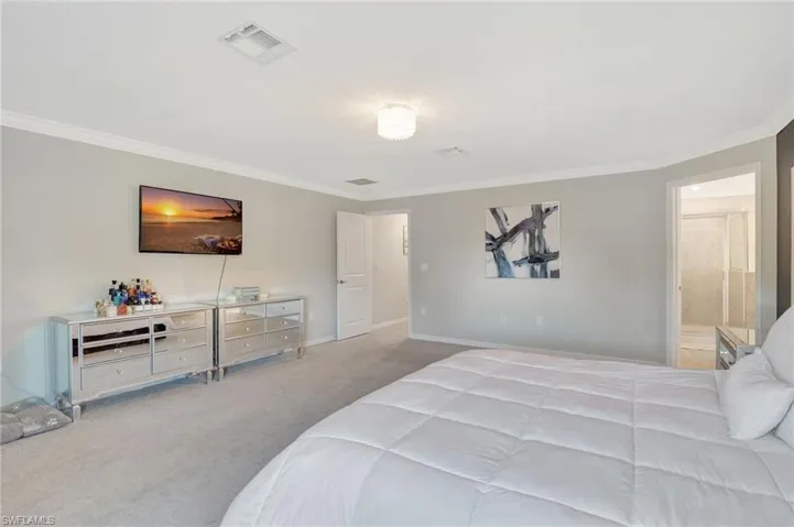 Carpeted bedroom featuring baseboards, visible vents, and ornamental molding