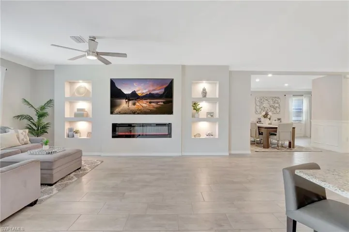 Living area featuring ornamental molding, built in shelves, visible vents, a glass covered fireplace, and ceiling fan