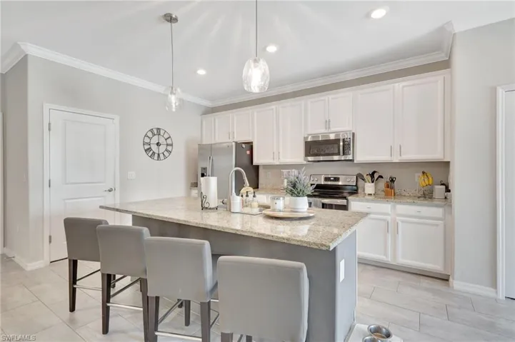 Kitchen with white cabinetry, a kitchen breakfast bar, ornamental molding, and appliances with stainless steel finishes