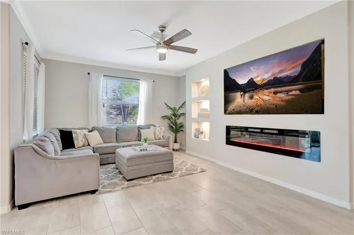 Living area with built in features, a glass covered fireplace, baseboards, and ceiling fan