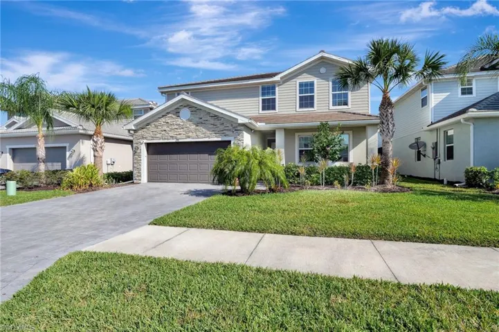 Traditional-style home with driveway, a front yard, a tile roof, stone siding, and a garage