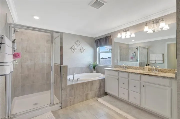 Bathroom featuring a sink, a stall shower, a garden tub, visible vents, and double vanity