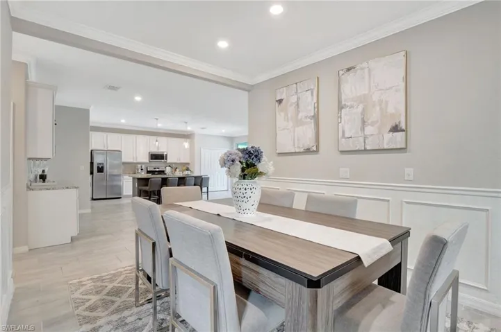 Dining room with light wood-style flooring, recessed lighting, ornamental molding, a wainscoted wall, and a decorative wall