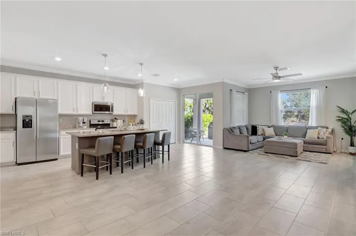 Kitchen featuring stainless steel appliances, white cabinetry, an island with sink, open floor plan, and a kitchen breakfast bar