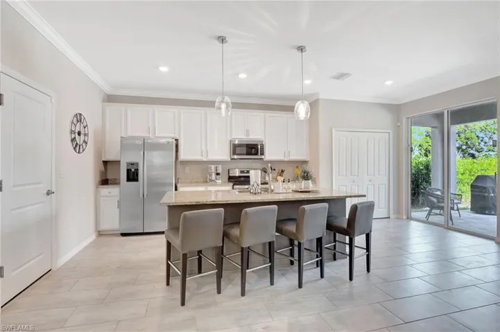 Kitchen featuring white cabinetry, light stone countertops, a breakfast bar, a kitchen island with sink, and appliances with stainless steel finishes