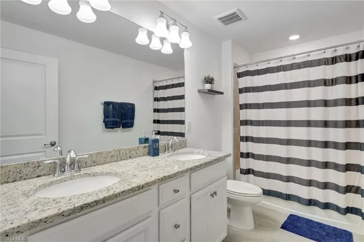Full bath with toilet, a sink, double vanity, and visible vents