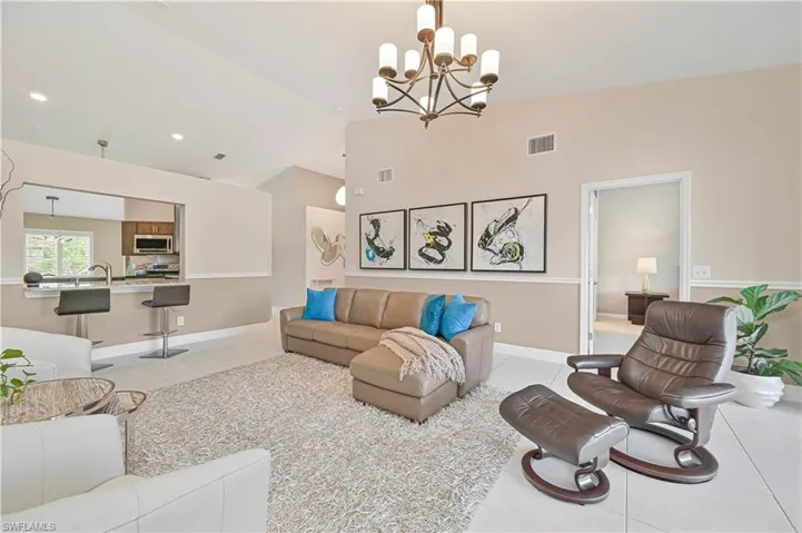 Living room featuring light tile patterned flooring, visible vents, high vaulted ceiling, and a notable chandelier