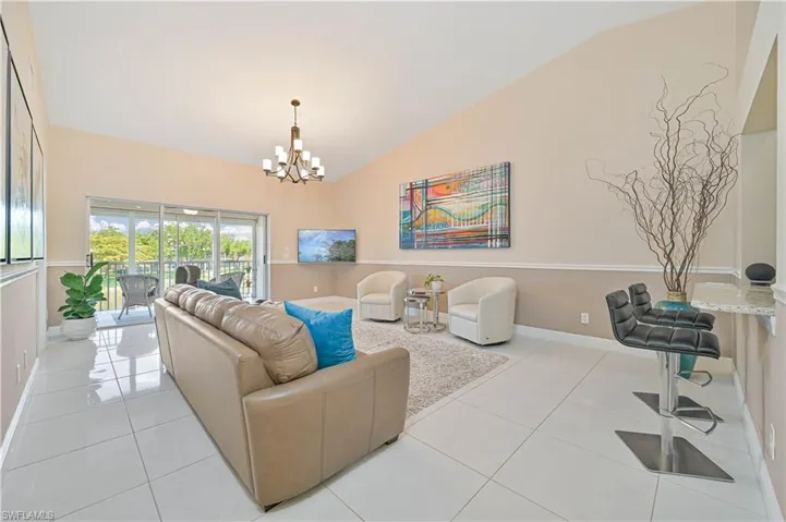 Living room with lofted ceiling, baseboards, a notable chandelier, and light tile patterned floors