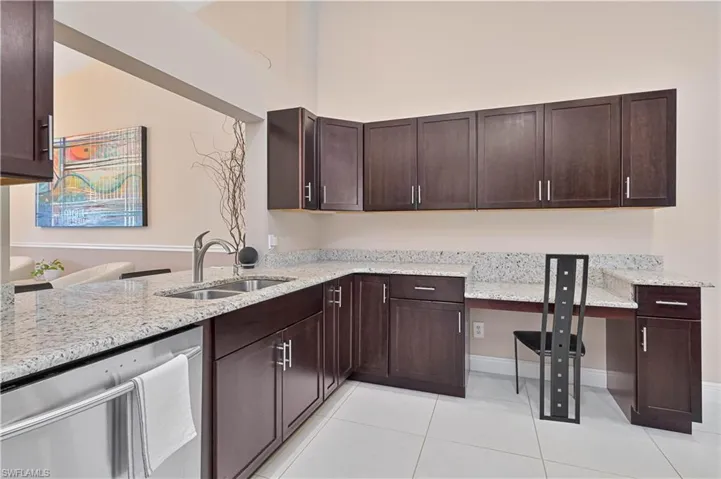 Kitchen with stainless steel dishwasher, dark brown cabinets, a sink, and light stone countertops