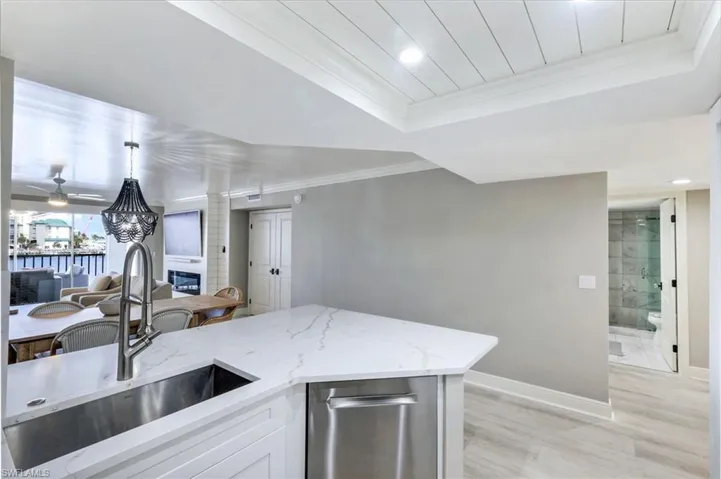 Kitchen with light stone counters, light wood-type flooring, white cabinets, a tray ceiling, and open floor plan