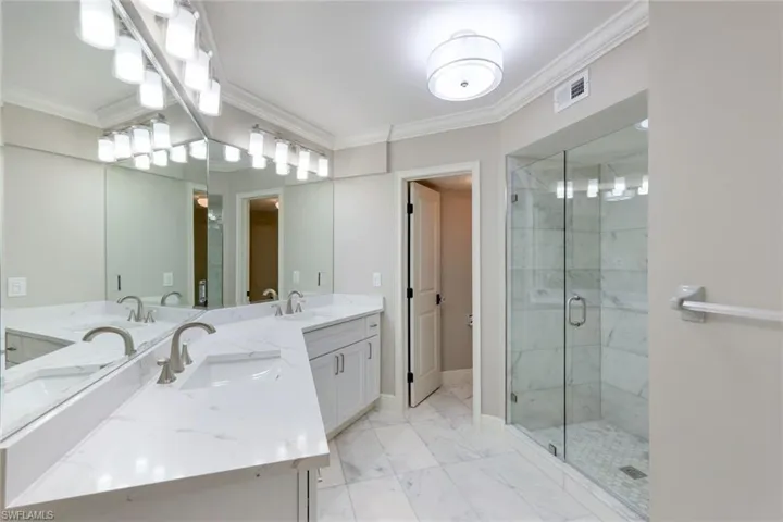 Bathroom featuring crown molding, a shower stall, double vanity, and light marble finish flooring