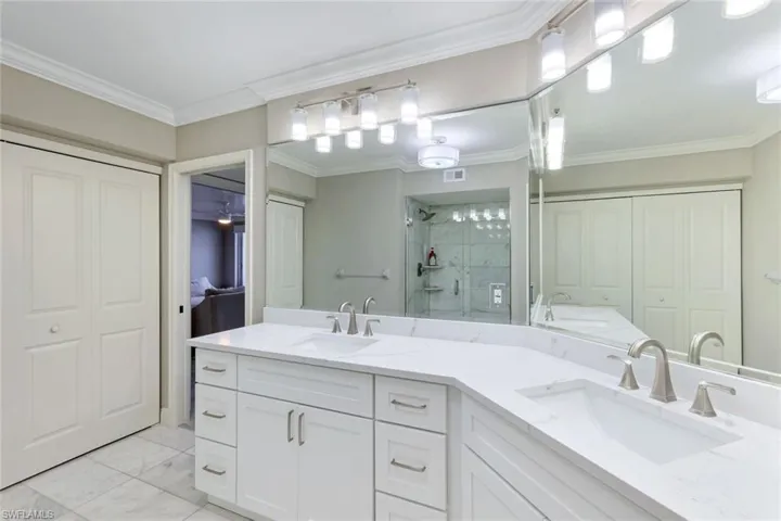 Ensuite bathroom featuring a closet, double vanity, a stall shower, ornamental molding, and light marble finish flooring