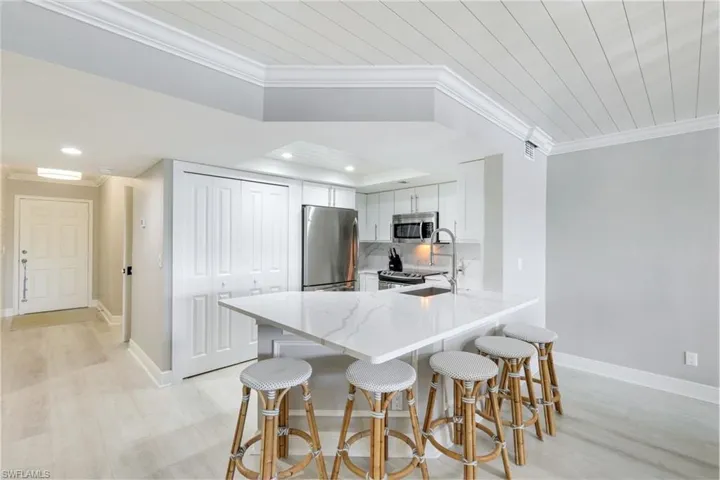 Kitchen featuring ornamental molding, light stone counters, a kitchen breakfast bar, stainless steel appliances, and white cabinets