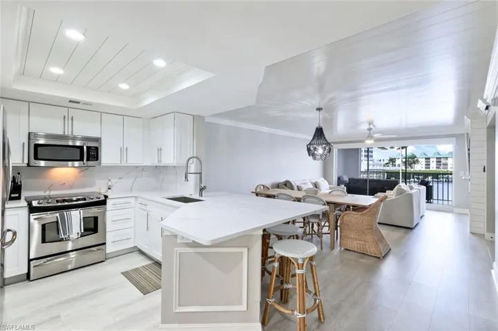 Kitchen featuring stainless steel appliances, a peninsula, backsplash, white cabinets, and a breakfast bar