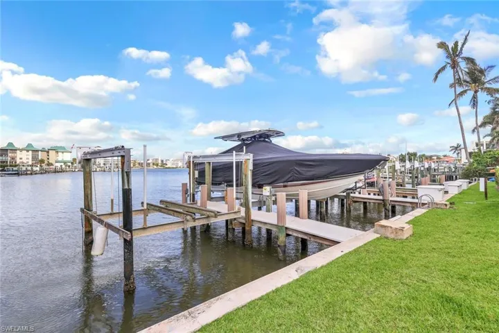 Dock with boat lift, a water view, and a lawn