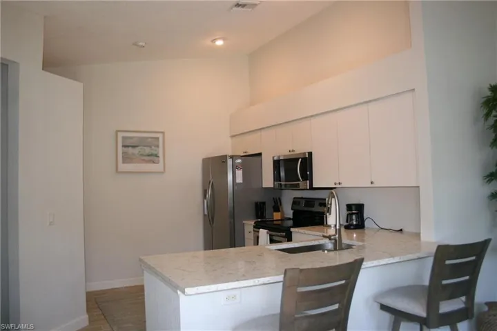 Kitchen featuring vaulted ceilings, light-toned cabinetry, stainless steel appliances, a breakfast bar, and light-toned countertops
